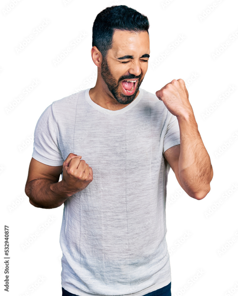 Young hispanic man with beard wearing casual grey t shirt celebrating surprised and amazed for success with arms raised and eyes closed Young hispanic man with beard wearing casual grey t shirt celebrating surprised and amazed for success with arms raised and eyes closed