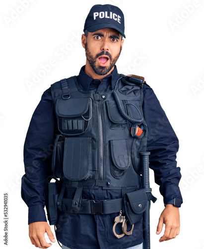Young hispanic man wearing police uniform in shock face, looking skeptical and sarcastic, surprised with open mouth