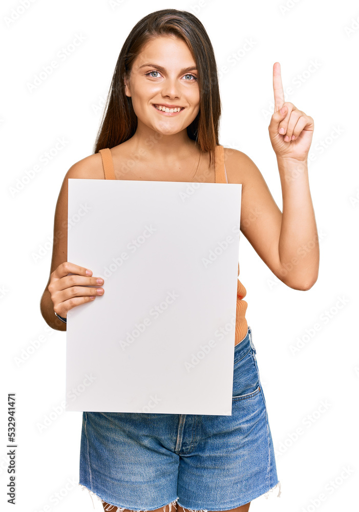 Young caucasian woman holding blank empty banner surprised with an idea or question pointing finger with happy face, number one Young caucasian woman holding blank empty banner surprised with an idea or question pointing finger with happy face, number one