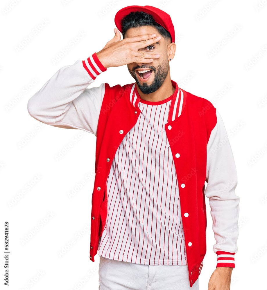 Young man with beard wearing baseball uniform peeking in shock covering face and eyes with hand, looking through fingers with embarrassed expression. Young man with beard wearing baseball uniform peeking in shock covering face and eyes with hand, looking through fingers with embarrassed expression.