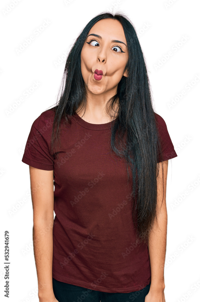 Fototapeta premium Young hispanic girl wearing casual t shirt making fish face with lips, crazy and comical gesture. funny expression.