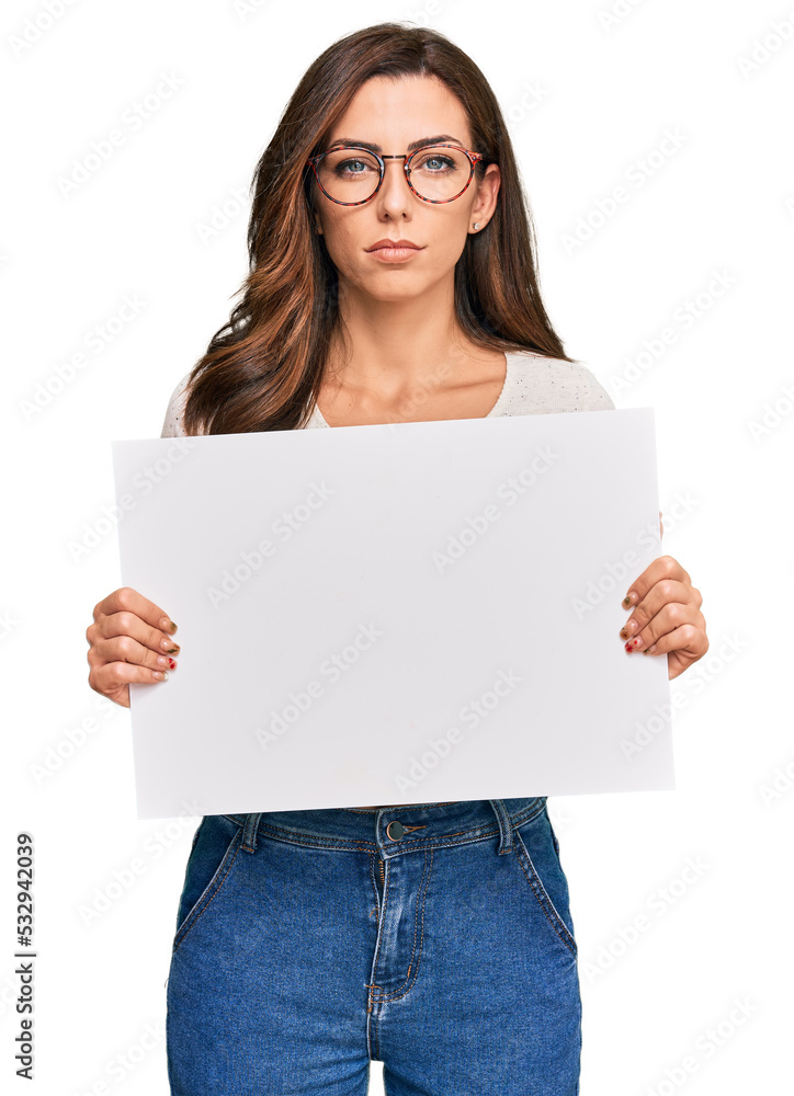 Young brunette woman holding blank empty banner thinking attitude and sober expression looking self confident Young brunette woman holding blank empty banner thinking attitude and sober expression looking self confident