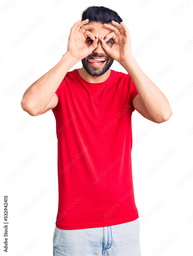 Fototapeta premium Young handsome man with beard wearing casual t-shirt doing ok gesture like binoculars sticking tongue out, eyes looking through fingers. crazy expression.