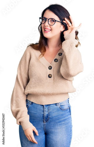 Beautiful young brunette woman wearing casual clothes and glasses smiling with hand over ear listening an hearing to rumor or gossip. deafness concept.