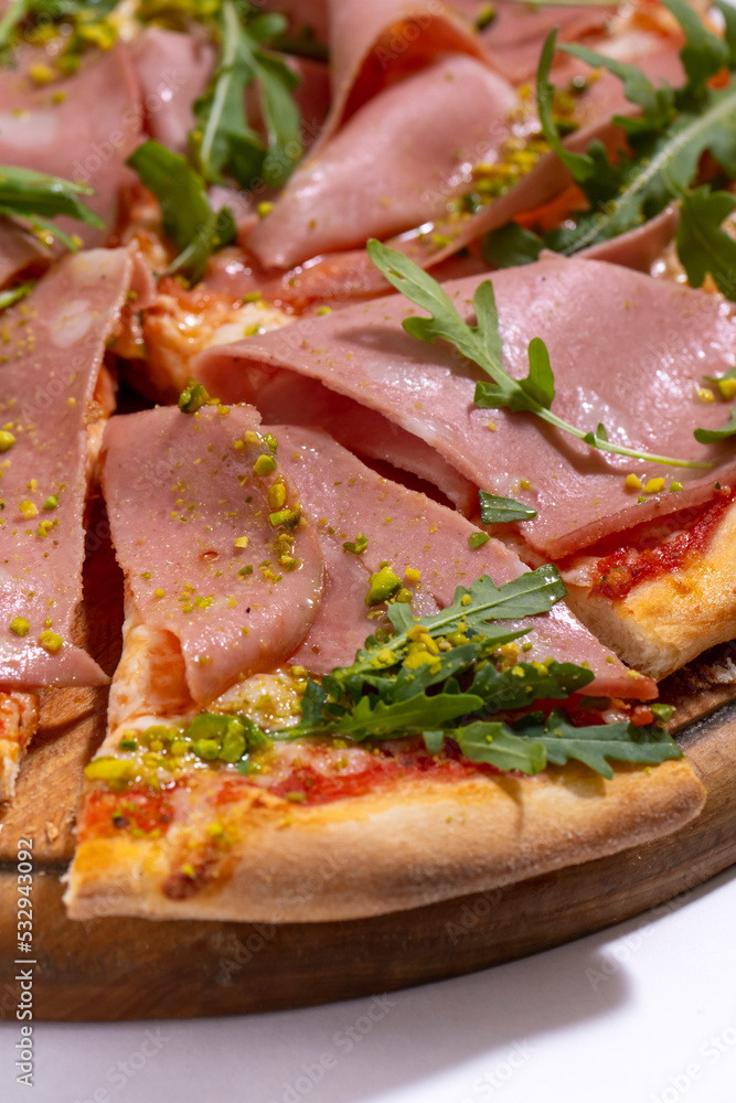 Pizza with ham, arugula and pistachios served on wooden platter