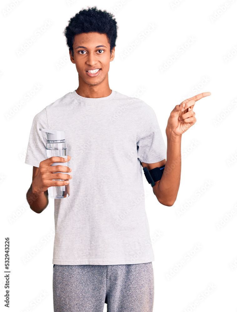 Young african american man wearing sportswear holding water bottle smiling happy pointing with hand and finger to the side Young african american man wearing sportswear holding water bottle smiling happy pointing with hand and finger to the side