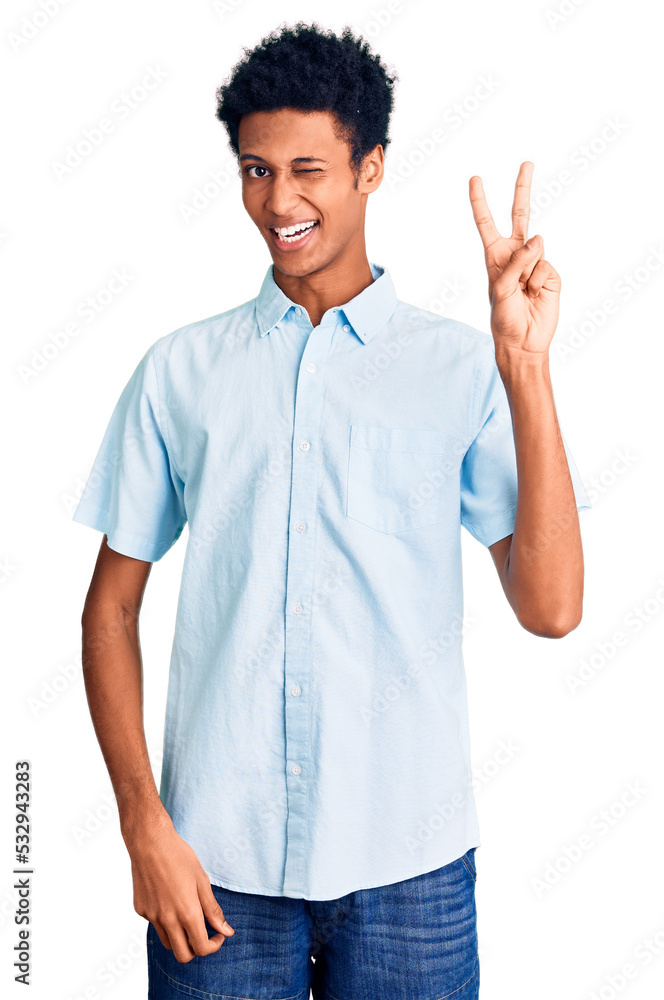 Young african american man wearing casual clothes smiling with happy face winking at the camera doing victory sign with fingers. number two. Young african american man wearing casual clothes smiling with happy face winking at the camera doing victory sign with fingers. number two.