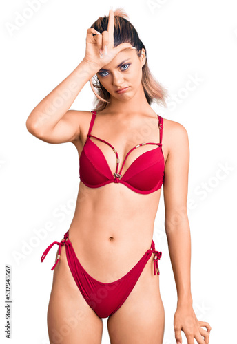 Young beautiful woman wearing bikini making fun of people with fingers on forehead doing loser gesture mocking and insulting. © Krakenimages.com