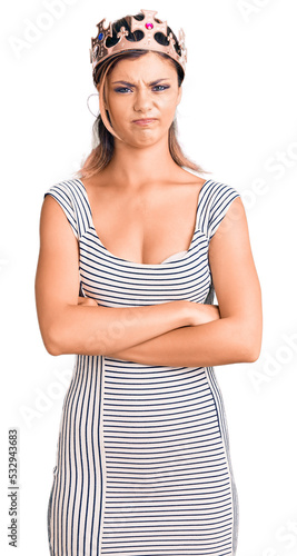 Young beautiful woman wearing king crown skeptic and nervous, disapproving expression on face with crossed arms. negative person.