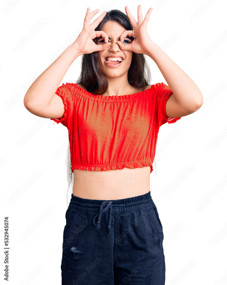 Brunette teenager girl wearing casual clothes doing ok gesture like binoculars sticking tongue out, eyes looking through fingers. crazy expression. Brunette teenager girl wearing casual clothes doing ok gesture like binoculars sticking tongue out, eyes looking through fingers. crazy expression.