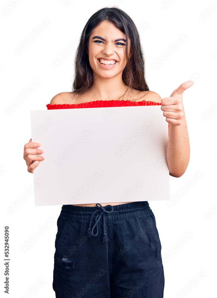 Brunette teenager girl holding blank empty banner smiling happy and positive, thumb up doing excellent and approval sign Brunette teenager girl holding blank empty banner smiling happy and positive, thumb up doing excellent and approval sign