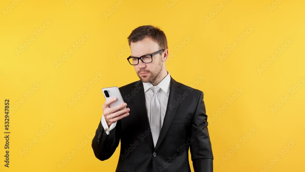 Handsome concentrated man in suit using mobile phone isolated over yellow background. Businessman chatting using mobile phone. 4K, UHD Handsome concentrated man in suit using mobile phone isolated over yellow background. Businessman chatting using mobile phone. 4K, UHD