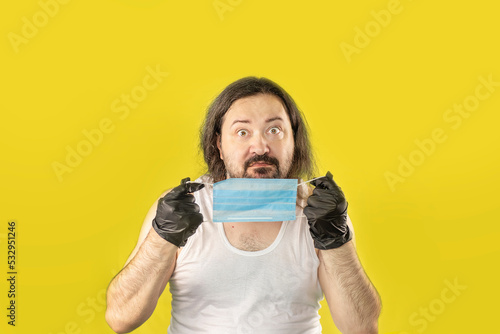 A confident, unshaven man in a white undershirt demonstrates a protective mask. An unemployed, unkemptly dressed adult from Eastern Europe.