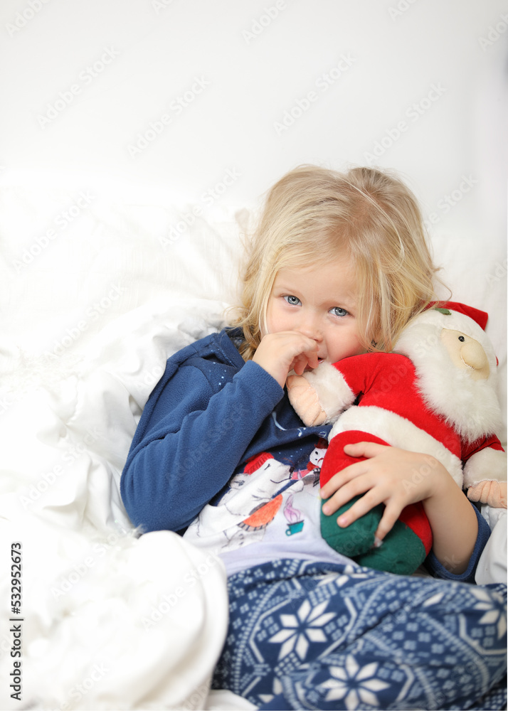 Cute little girl is very surprised and excited, lying on white background and holding little santa claus, looking straight. Christmas holiday