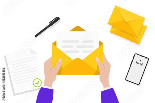 Hands holding an opened envelope. Hands holding letter, surrounded by papers, pen, envelope and phone. Top view on table surface. Sending letter through postal service. Mail delivery and post office