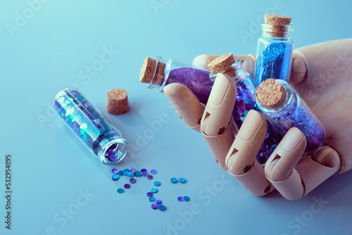 Glitter powder, glittering product bottles in ooden dummy hand, artificial artistic wood model hand. Spilled glitter particles on table. Makeup, craft or other hobby supplies in neon colors.