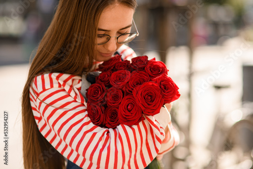 Close-up view bouquet of red rose which tenderly holding young woman and look at it