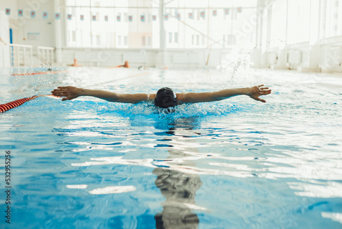 Professional sportswoman in cap swimming in pool and performing Butterfly stroke while competing in pool during race 