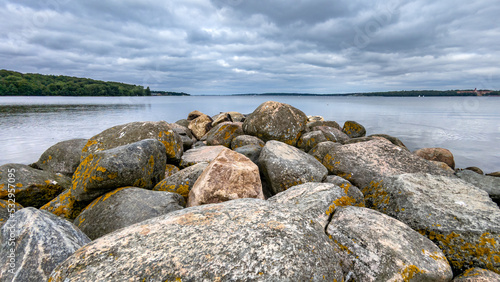 massive stones in the foreground. midground water. Background border with Denmark. Cloudy sky. Harrislee, Flensburg, Fjord, Baltic Sea, Germany