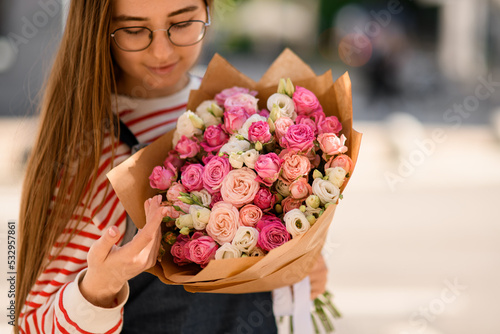 close-up view on young woman who tenderly holding bouquet of pink rose flowers and look at it