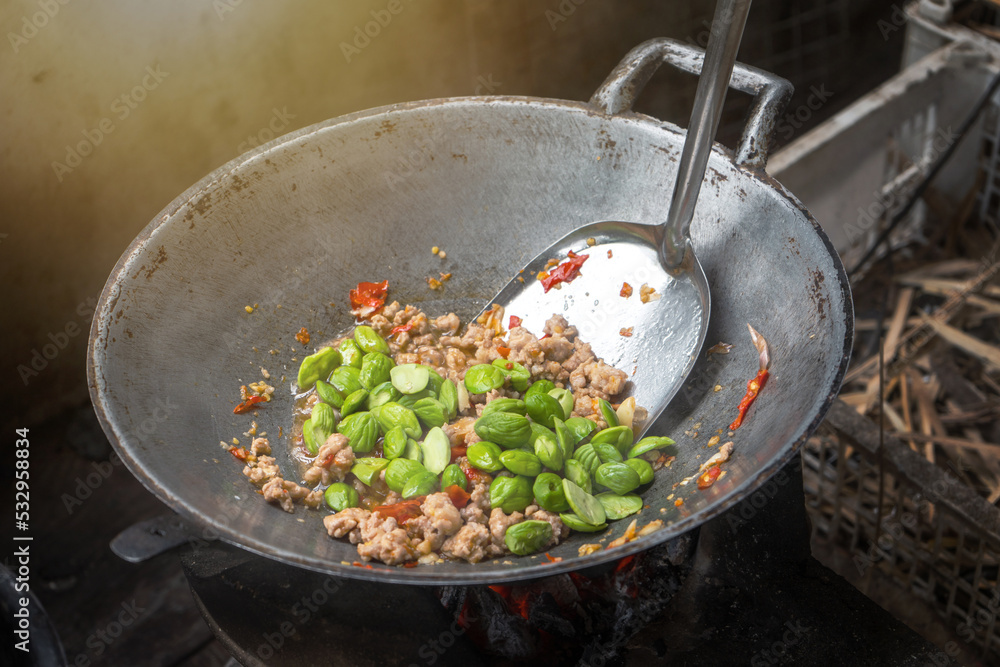 Cooking from local ingredients of Thailand. Stir-fried Stink Bean and Minced pork or Stir Fried Sato (Pakria) in an old pan on a charcoal stove. Cooking from local ingredients of Thailand. Stir-fried Stink Bean and Minced pork or Stir Fried Sato (Pakria) in an old pan on a charcoal stove.