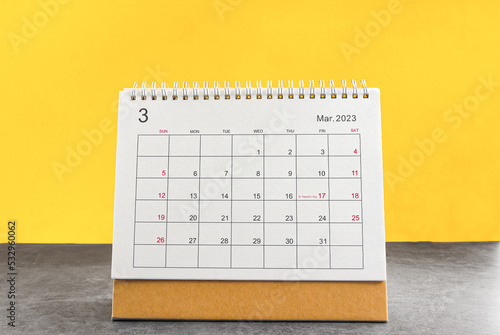 March calendar 2023 on the wooden table on a yellow background.