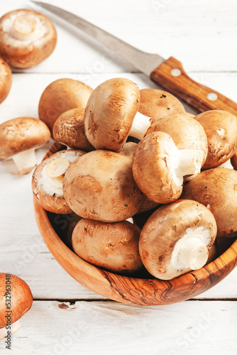 Fresh brown champignon mushrooms in wooden bowl, white wooden kitchen table, top view, copy space