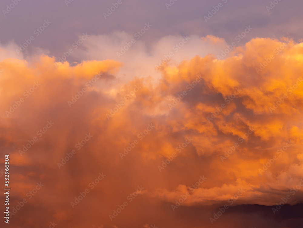 Colorful orange thunderstorm clouds at sunset time. Close-up of a beautiful cloudscape in the nature. Natural weather phenomenon in the sky. Abstract background of a dramatic sky.
