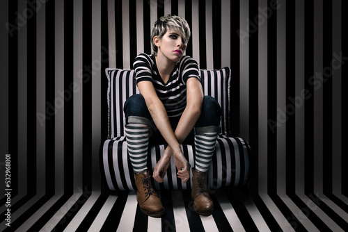 beautiful mexican model poses elegant and sensual for artsy portrait with stripes in black and white while sit on striped chair in front of stripe pattern wall background with black and white socks