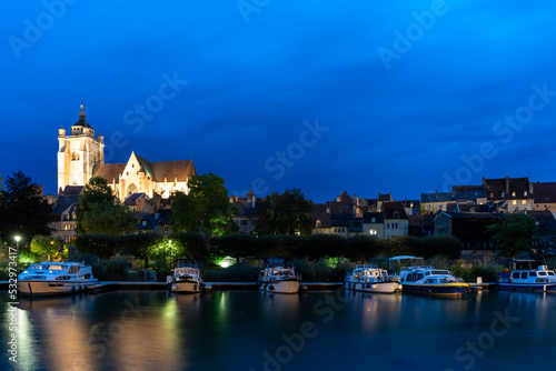 nightime view of the illuminated Notre Dame catholic church in Dole with houseboats on the Doubs River in the foreground