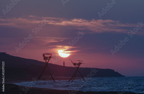 majestic sunrise over the sea against the backdrop of a lighthouse and fishing structures
