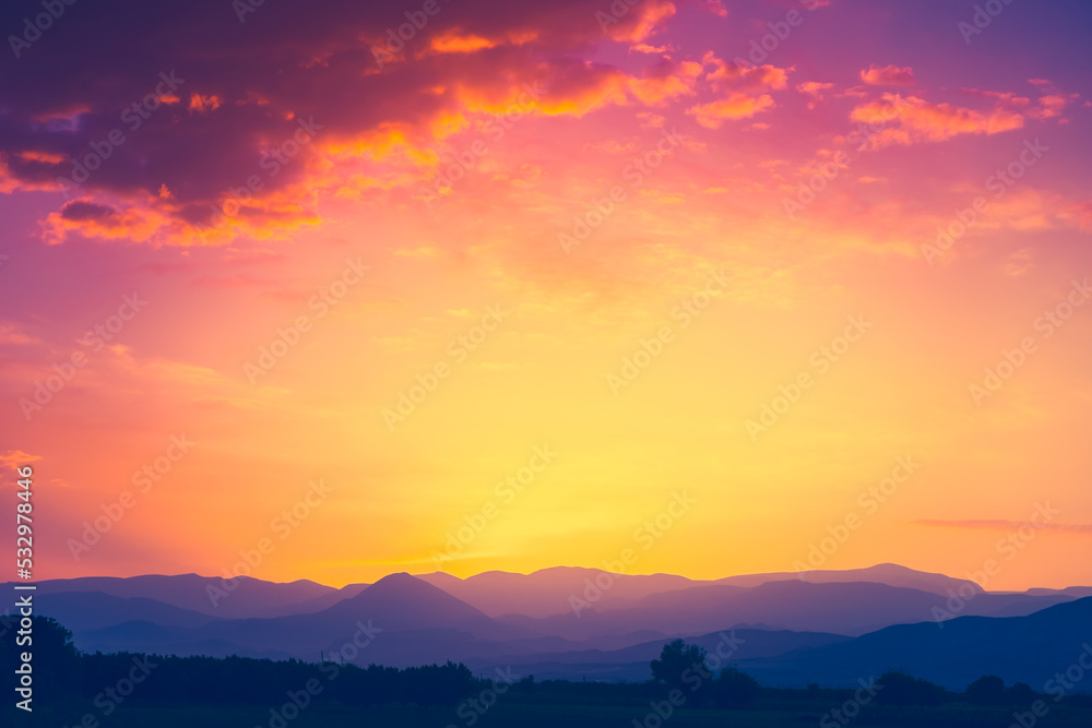 Beautiful mountain range with sunset sun in orange sky with colorful clouds. Amazing nature scenery. Natural texture and background