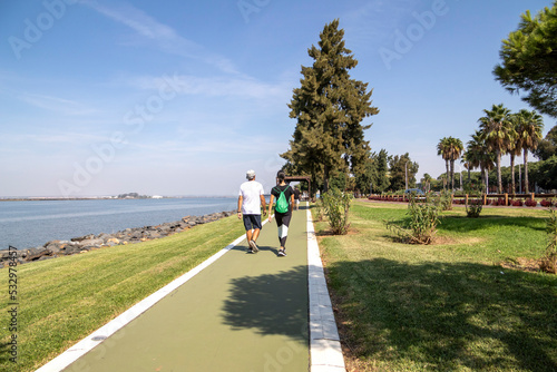 Woman with sportswear and man with sportswear, walking along the side of the river. View from behind. Healthy life concept.