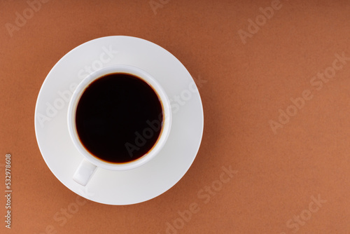 Coffee cup on a brown background. Cup of black coffee on a white saucer. Top view. Copy space