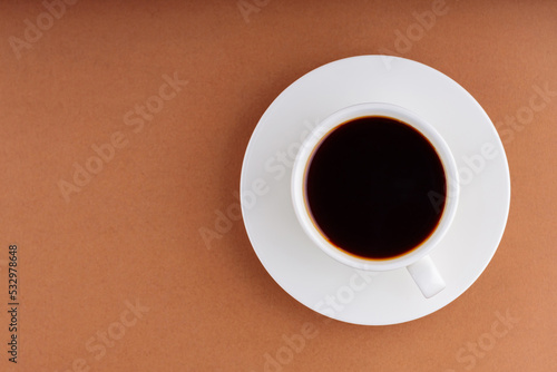 Coffee cup on a brown background. Cup of black coffee on a white saucer. Top view. Copy space