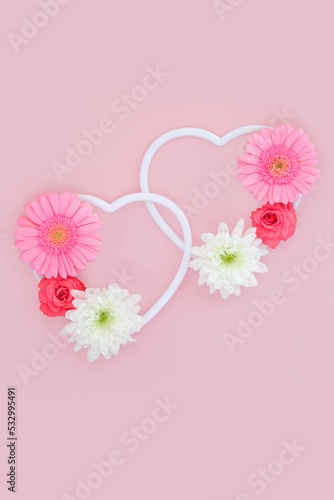 Creative Valentines Day concept with two hearts entwined decorated with rose, gerbera and chrysanthemum flowers. Minimal romantic love heart nature concept. On pink.