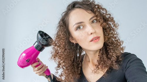 Girl Gets Her Hair Curly. Hair care concept. A curly woman dries her hair at home with a hair dryer with a diffuser nozzle. A beautiful white girl uses a modern pink hair dryer photo