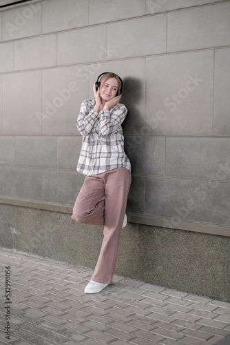 Happy teen  girl hipster  listening music with closed eyes, near urban wall  wearing headphones.  enjoying streaming service app outdoors. © lelechka