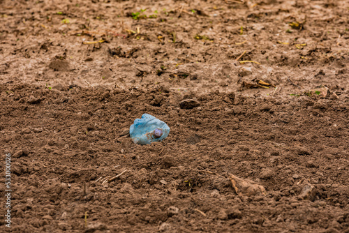 Illegal garbage disposal of a plastic bottle on the field in environment by litterer photo