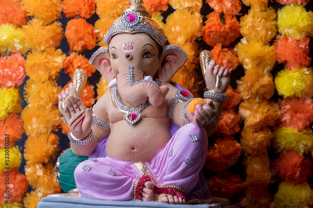 A Beautiful clay statue/Idol of an Indian god Lord Ganesha decorated with colourful Marigold garland 