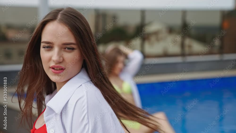 Beautiful brunette in red swimsuit and white shirt walks and turns in front of camera. Female model posing near the pool outdoors. Beautiful brunette in red swimsuit and white shirt walks and turns in front of camera. Female model posing near the pool outdoors.