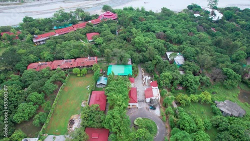 aerial drone shot showing the red roofs of resort nestled between green tress with swimming pool and cottages to the kosi dried riverbed located at jim corbett park in India photo