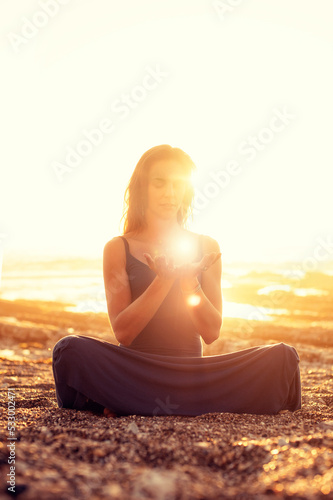 Beautiful woman sitting on a golden beach meditating on light energy. 
