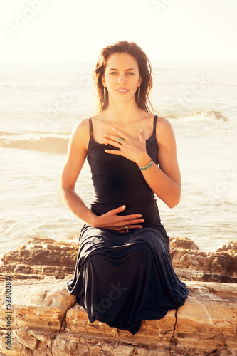 Embodiment By The Sea. Woman holding her center and heart in an emotionally energetic yoga posture.