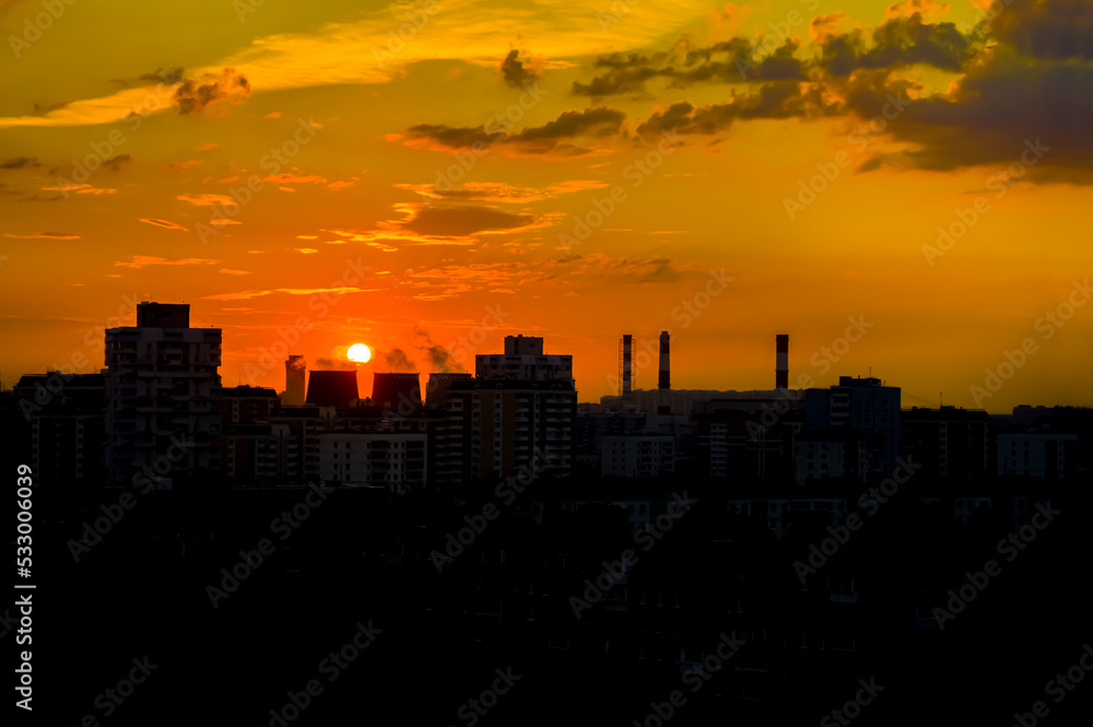 Bright colorful sunset, cloudy sky. Twilight, cityscape. Silhouettes of buildings, pipes and cooling towers of a thermal power plant against a bright sky. Moscow, evening landscape. Background Bright colorful sunset, cloudy sky. Twilight, cityscape. Silhouettes of buildings, pipes and cooling towers of a thermal power plant against a bright sky. Moscow, evening landscape. Background