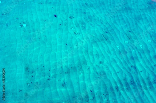 Waves underwater. Blue transparent water. The sand on the seabed repeats the waves of water. Under water pattern (vertical lines), nature draws, sea water background, wallpaper, texture, postcard