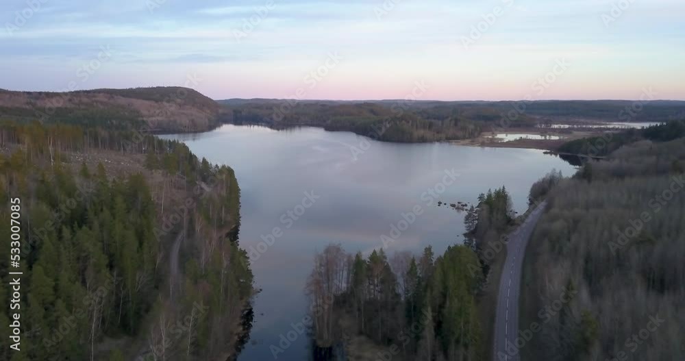 Drone flying over lake surounded by forest in sunset Drone flying over lake surounded by forest in sunset