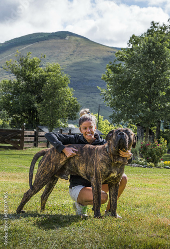 Smiling young woman hugging her dog Presa Canario outside in her garden