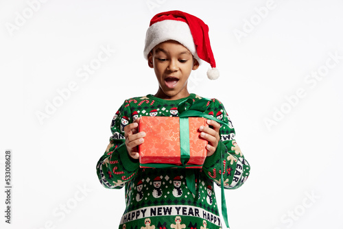 Happy smiling child in a knitted colorful sweater holds box in festive package. Boy rejoices at holiday, Christmas, New Year.