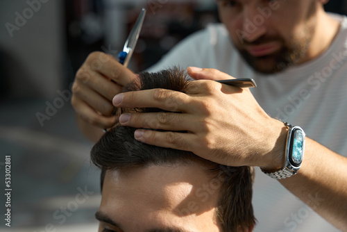 Skilled barber looking focused while trimming his client hair